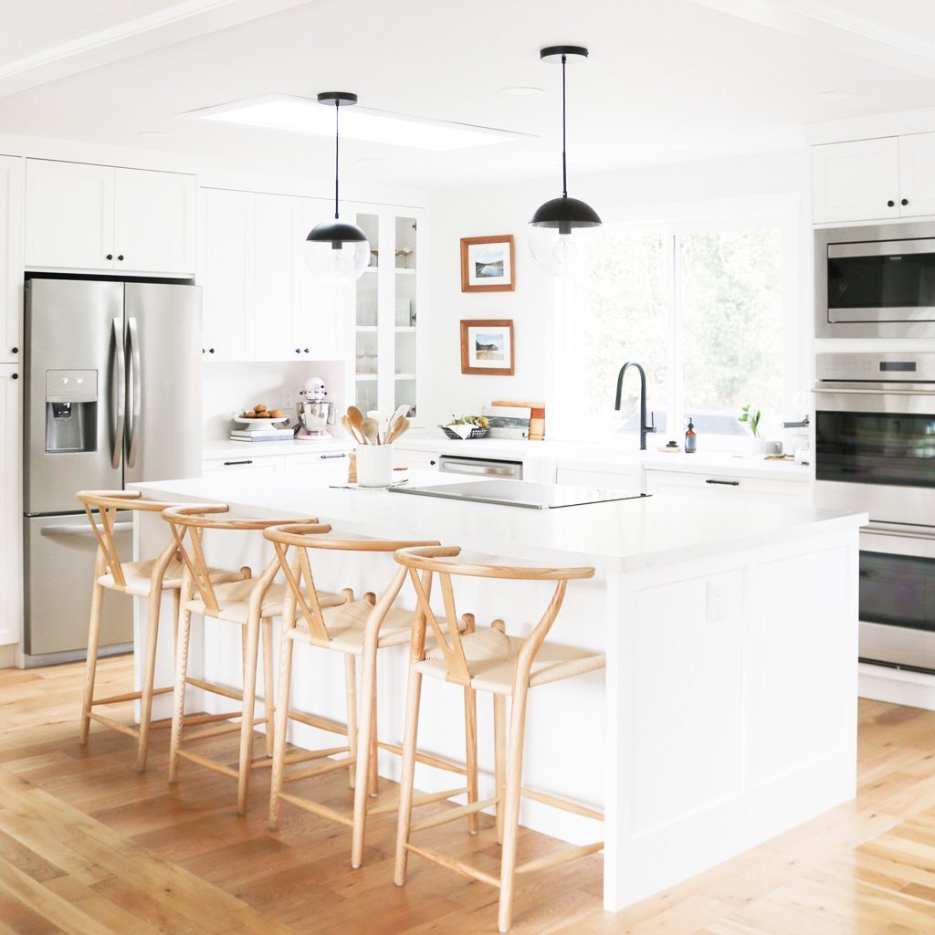 Three geometric metal pendant lights over a kitchen island with white cabinets and open shelves, four-bar stools along island.