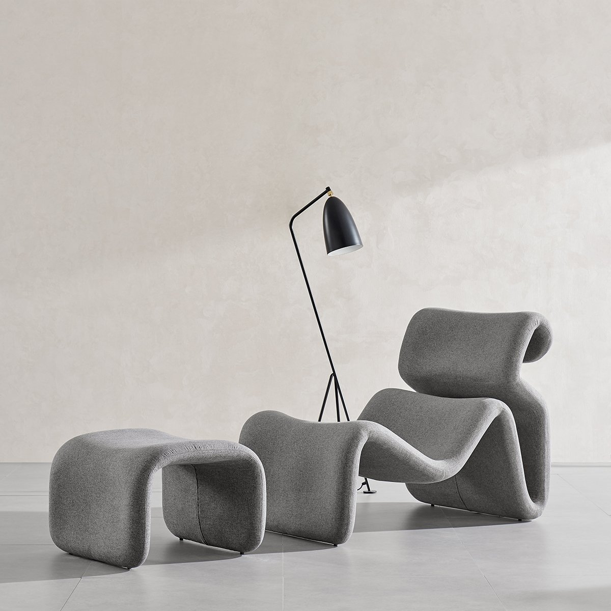 Grey sculptural lounge chair with curved wave form and separate small stool-like section