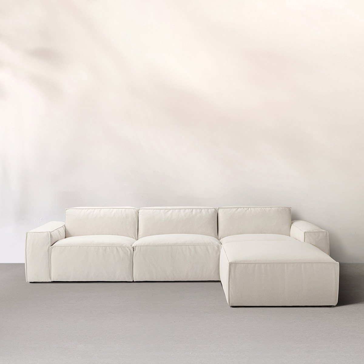 White three-seat sofa with plush cushions against pale backdrop.
