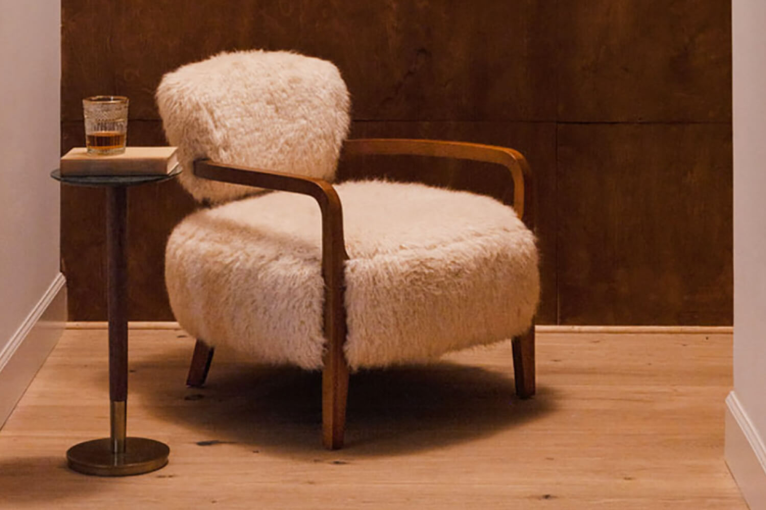 A cozy Yeti Sheepskin Armchair in a warm, well-lit room featuring fluffy upholstery for comfort and a small round side table holding a glass and a book.