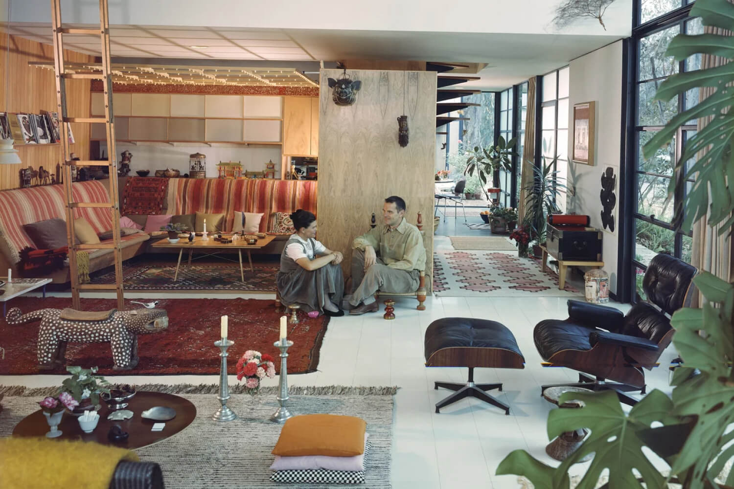 Charles Eames and his wife, Ray Eames, are sitting in their vividly mid-century modern home.