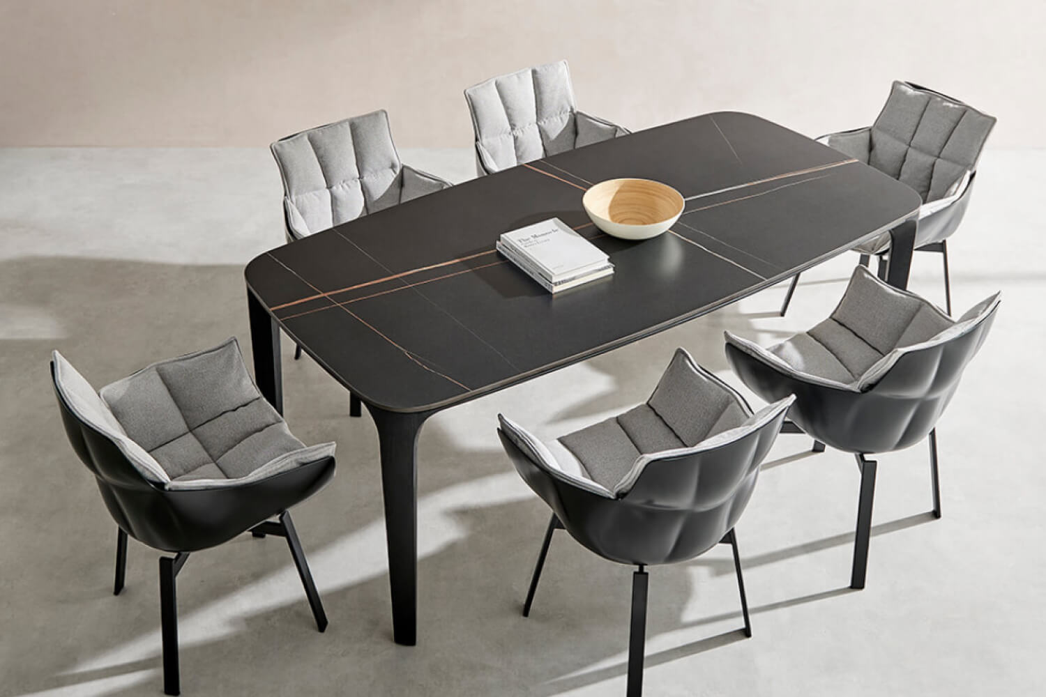 A modern dining area featuring the Myko Modern Rectangular Sintered Stone Dining Table. The table showcases a sleek black surface with subtle orange linear accents and six contemporary chairs upholstered in grey fabric.