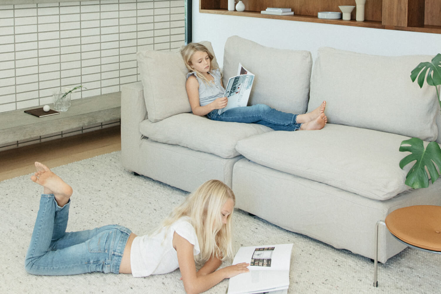 A well-lit, modern living space featuring an 'EM Sky Sofa' where two girls are relaxing and reading. 