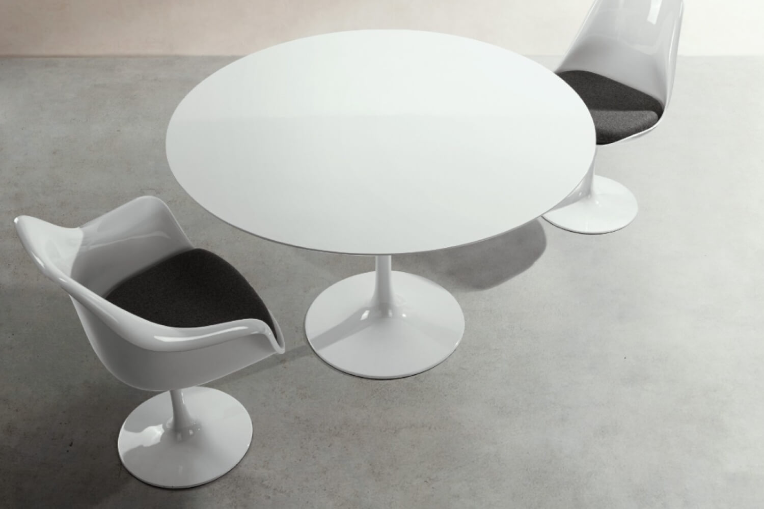 A modern dining setting featuring a white oval tulip table paired with two Tulip Armchairs made of fiberglass, showcasing a sleek design with a smooth white finish and contrasting black cushions, set against a subtle gray concrete floor.